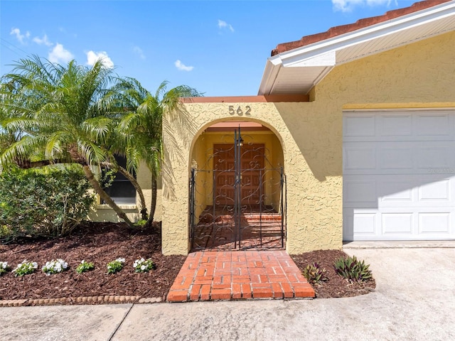 view of exterior entry featuring stucco siding, a garage, and a gate