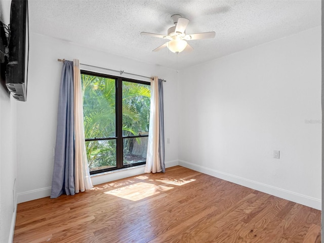 empty room featuring a textured ceiling, wood finished floors, baseboards, and ceiling fan