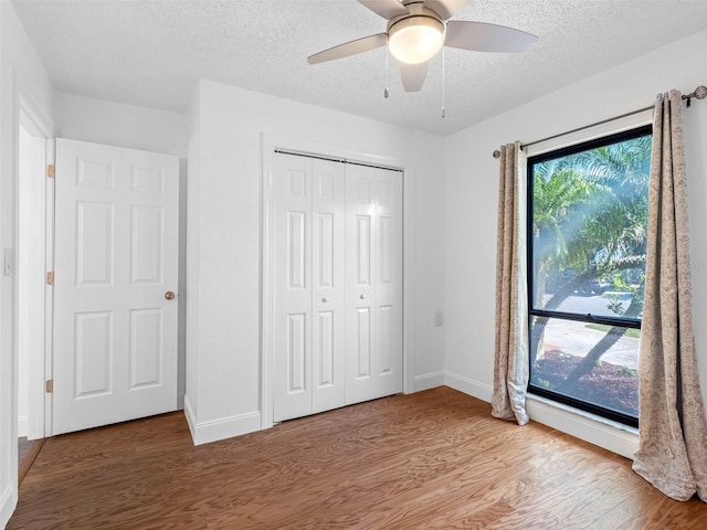 unfurnished bedroom featuring a closet, a textured ceiling, baseboards, and wood finished floors