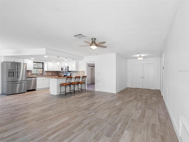 unfurnished living room featuring light wood finished floors, visible vents, a textured ceiling, and a ceiling fan