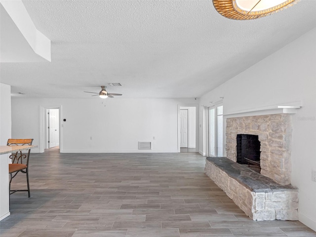 unfurnished living room featuring wood finish floors, visible vents, a ceiling fan, and a fireplace