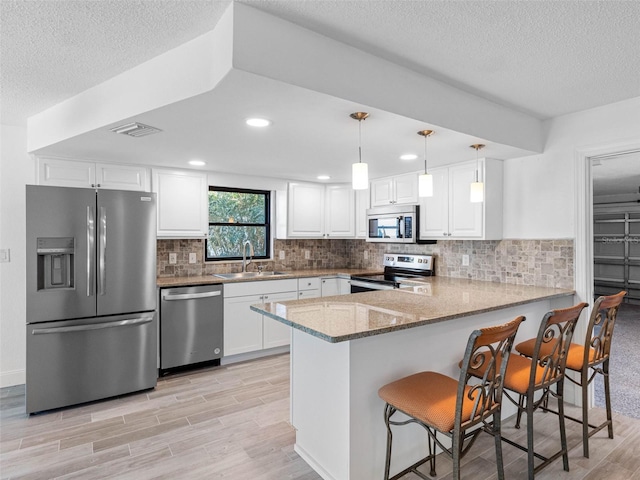 kitchen with a peninsula, a sink, decorative backsplash, stainless steel appliances, and white cabinets