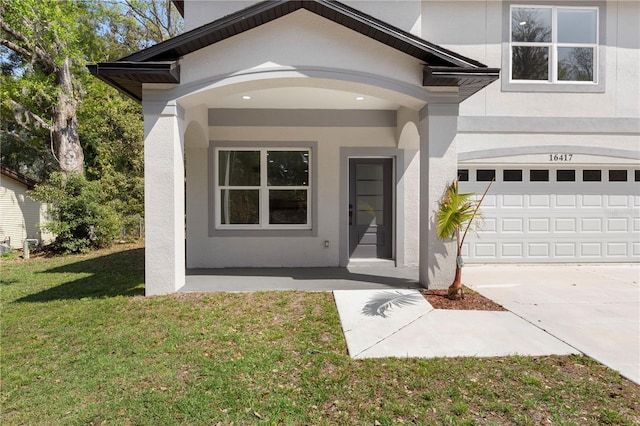 entrance to property featuring stucco siding, a lawn, a garage, and concrete driveway