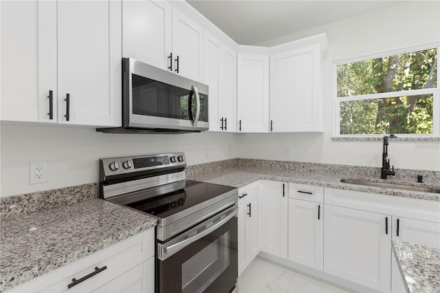 kitchen featuring stainless steel appliances, marble finish floor, a sink, light stone counters, and white cabinets