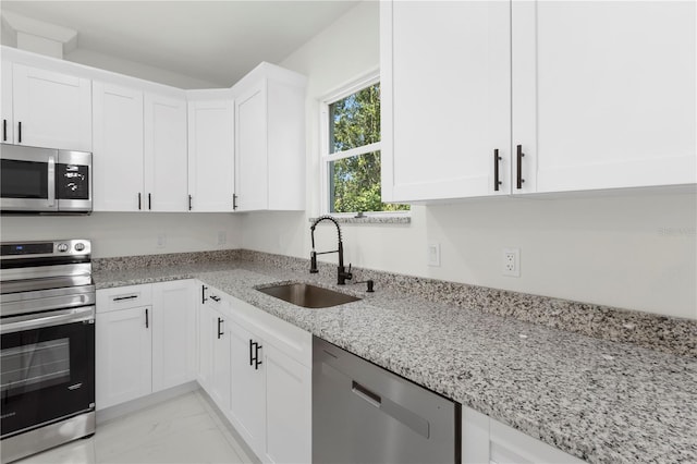 kitchen with light stone counters, a sink, white cabinetry, stainless steel appliances, and marble finish floor