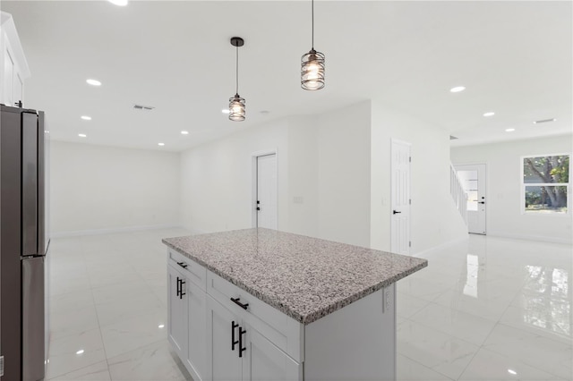 kitchen featuring light stone counters, freestanding refrigerator, a center island, hanging light fixtures, and open floor plan