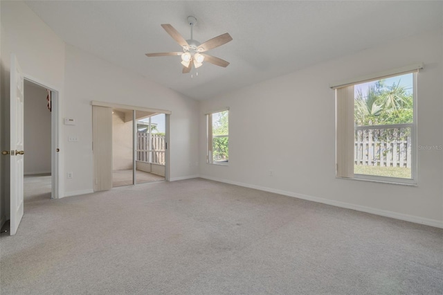 empty room with a ceiling fan, vaulted ceiling, light colored carpet, and baseboards
