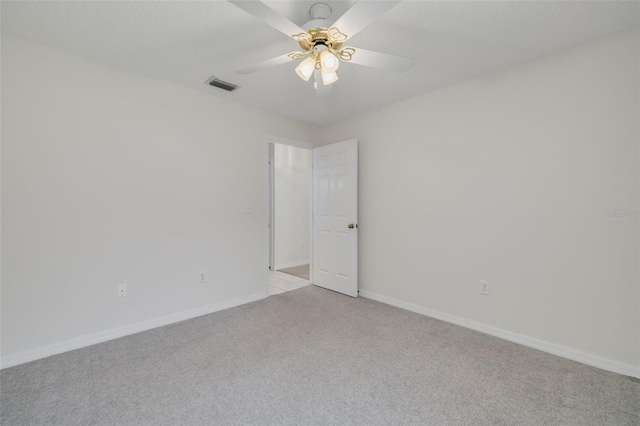 spare room with baseboards, visible vents, a ceiling fan, and light carpet