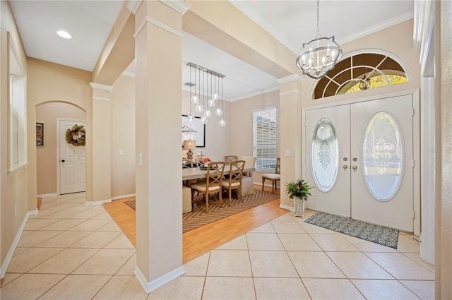 entrance foyer with light tile patterned floors, decorative columns, an inviting chandelier, and ornamental molding