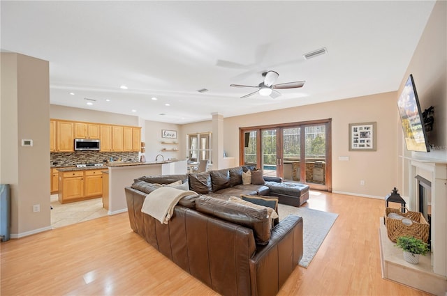 living area with a ceiling fan, visible vents, baseboards, light wood-style floors, and a glass covered fireplace