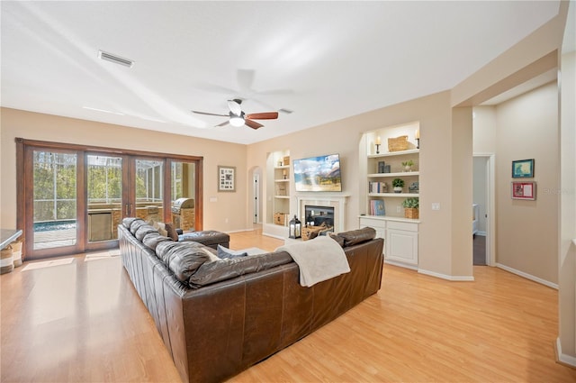 living area featuring visible vents, light wood-style flooring, a glass covered fireplace, baseboards, and ceiling fan