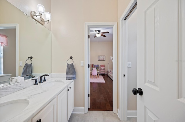 ensuite bathroom featuring double vanity, connected bathroom, a ceiling fan, and a sink