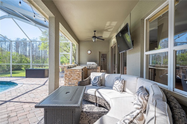 view of patio featuring glass enclosure, an outdoor kitchen, ceiling fan, a sink, and an outdoor hangout area