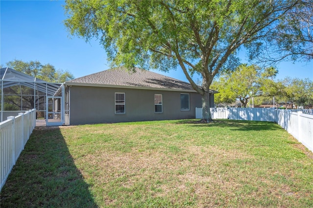 back of house with stucco siding, a lawn, a fenced backyard, roof with shingles, and a lanai