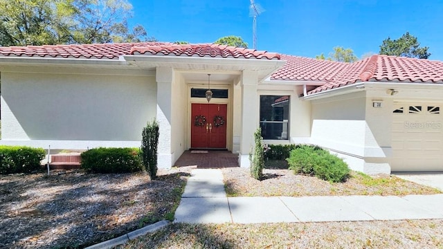 property entrance with stucco siding, an attached garage, and a tiled roof