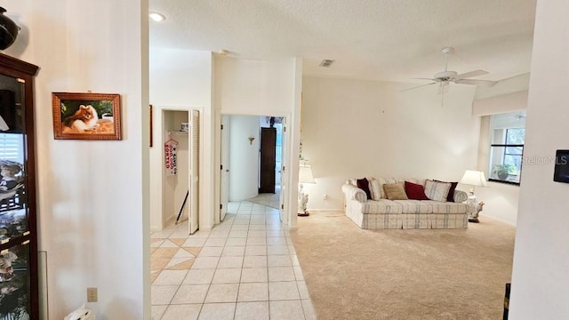 living area featuring visible vents, light carpet, light tile patterned floors, a textured ceiling, and a ceiling fan