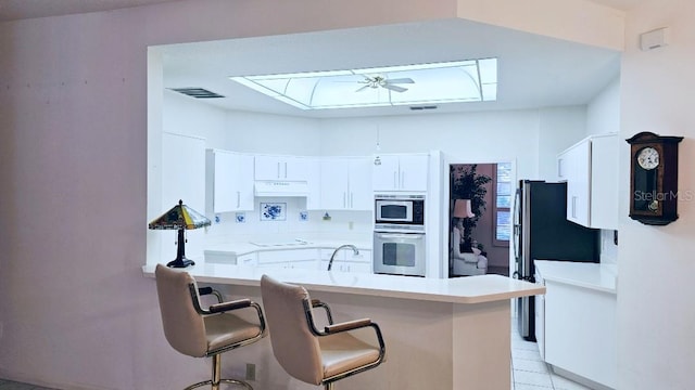 kitchen with a ceiling fan, a breakfast bar, a peninsula, appliances with stainless steel finishes, and under cabinet range hood