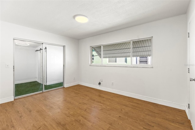 unfurnished bedroom featuring wood finished floors, baseboards, a closet, and a textured ceiling