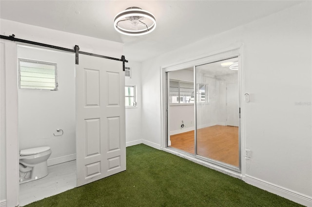 unfurnished bedroom featuring a barn door, baseboards, a closet, and carpet flooring