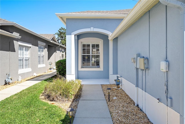 view of exterior entry featuring a shingled roof and stucco siding