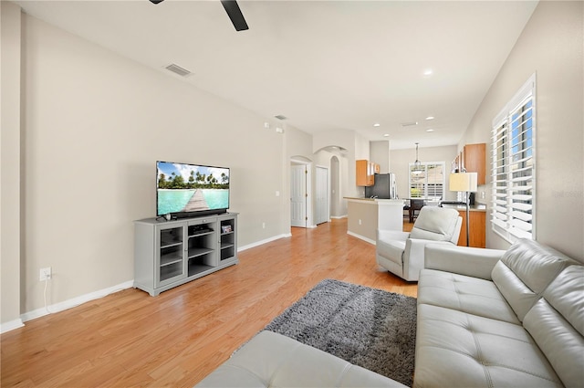 living area with a ceiling fan, visible vents, baseboards, light wood-style flooring, and arched walkways