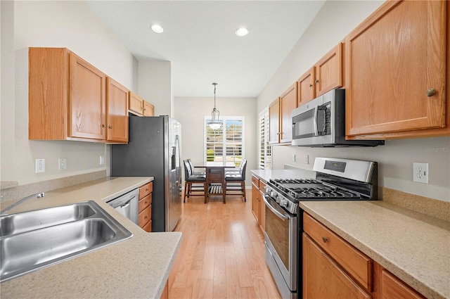 kitchen featuring a sink, light wood-style floors, appliances with stainless steel finishes, light countertops, and hanging light fixtures