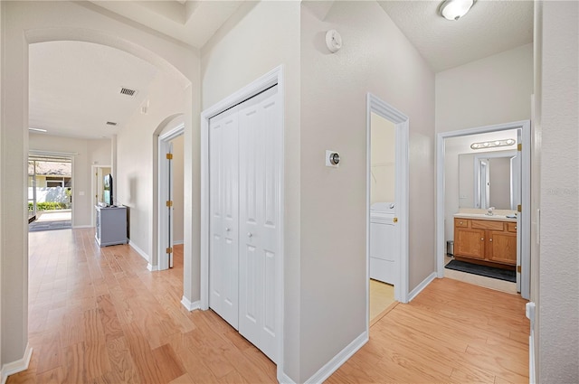 corridor featuring visible vents, light wood-style flooring, baseboards, and arched walkways