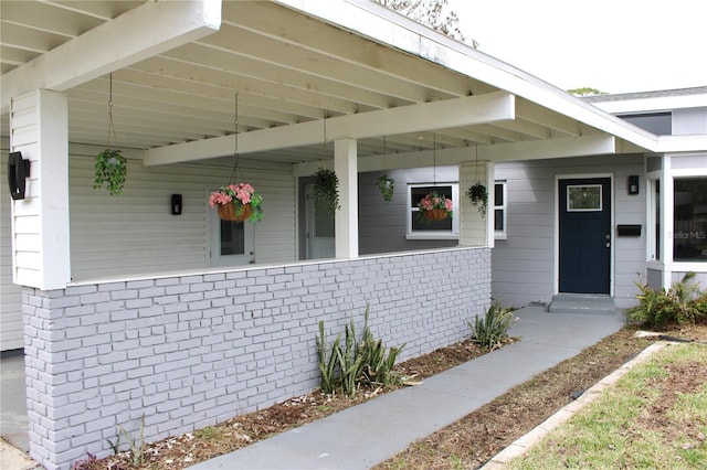 view of exterior entry with brick siding and a porch