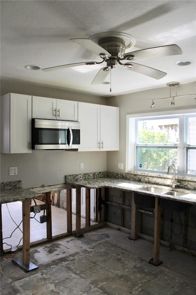 kitchen with white cabinetry, stainless steel microwave, light stone counters, and a sink