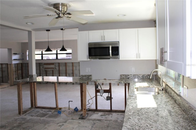 kitchen with light stone countertops, plenty of natural light, a sink, white cabinets, and stainless steel microwave