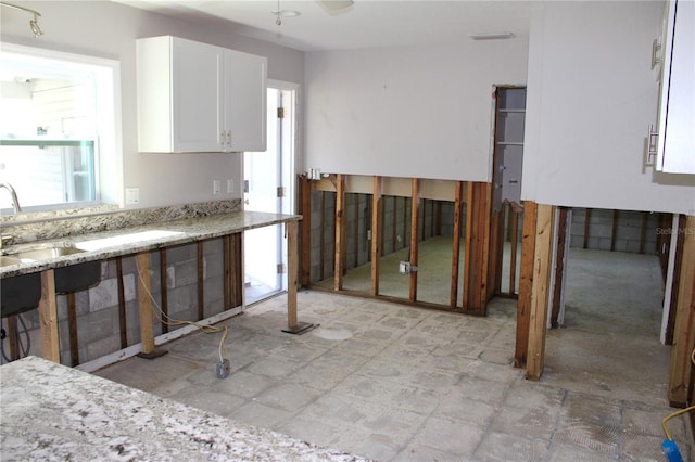 kitchen featuring a sink, light stone counters, and white cabinetry