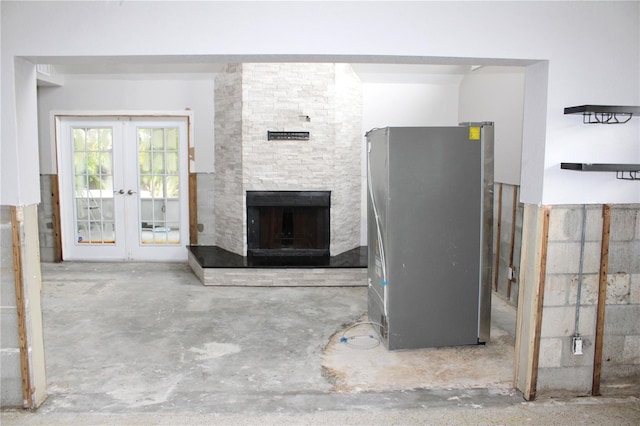 unfurnished living room featuring french doors, unfinished concrete flooring, and a stone fireplace