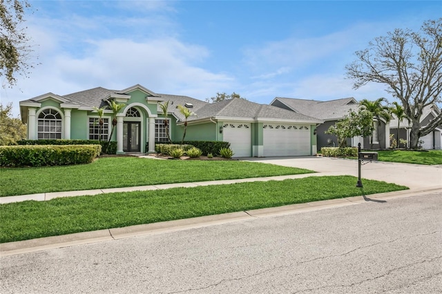 view of front of property featuring a front yard, roof with shingles, driveway, an attached garage, and stucco siding