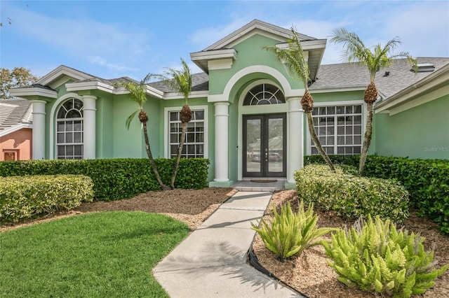 entrance to property featuring french doors, a shingled roof, and stucco siding