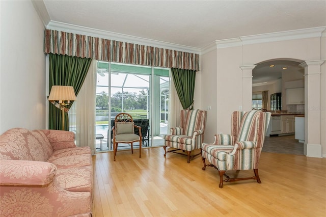 living area featuring light wood finished floors, arched walkways, ornate columns, and ornamental molding