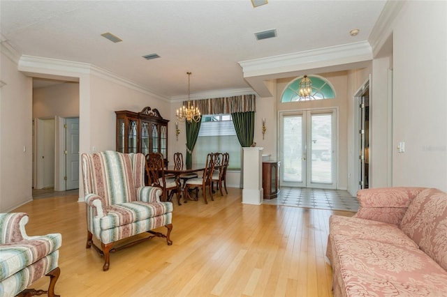 living room featuring light wood finished floors, a notable chandelier, visible vents, and ornamental molding