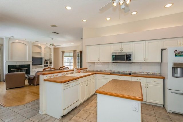 kitchen with a sink, a glass covered fireplace, white appliances, light tile patterned flooring, and ceiling fan