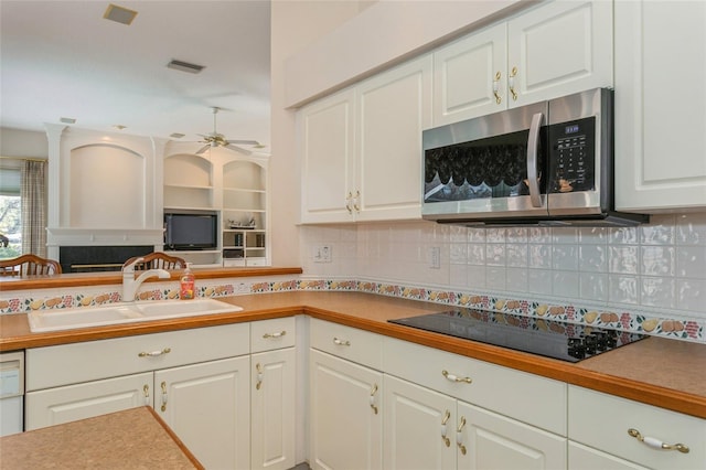 kitchen with a sink, stainless steel microwave, white cabinetry, decorative backsplash, and black electric stovetop