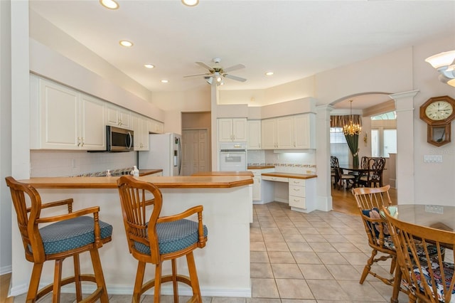 kitchen featuring a kitchen breakfast bar, a peninsula, arched walkways, white appliances, and ornate columns