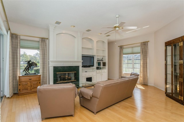 living area with a tiled fireplace, light wood-style flooring, baseboards, and a ceiling fan