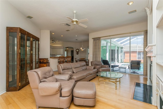 living room with arched walkways, visible vents, light wood finished floors, and ceiling fan