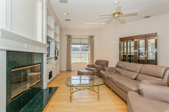 living room with visible vents, baseboards, light wood-type flooring, a tile fireplace, and a ceiling fan