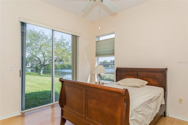 bedroom with baseboards, a water view, light wood-style floors, and access to outside