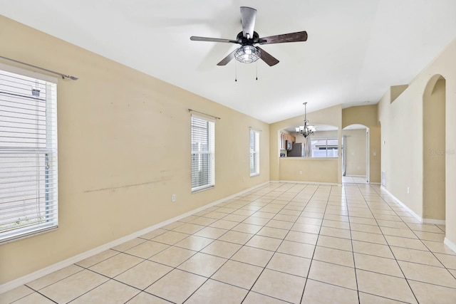 empty room with baseboards, lofted ceiling, light tile patterned floors, ceiling fan with notable chandelier, and arched walkways