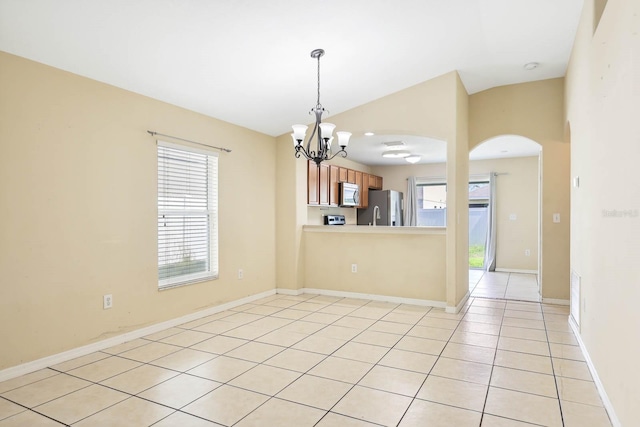 empty room featuring light tile patterned floors, a notable chandelier, a wealth of natural light, and vaulted ceiling