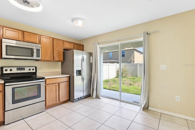 kitchen featuring light tile patterned floors, stainless steel appliances, brown cabinetry, and light countertops