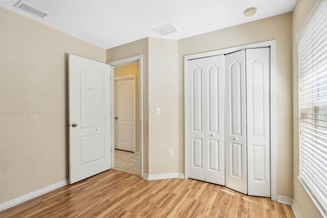 unfurnished bedroom with a closet, visible vents, baseboards, and light wood-style floors