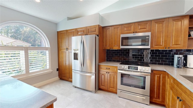 kitchen with brown cabinetry, backsplash, stainless steel appliances, and lofted ceiling