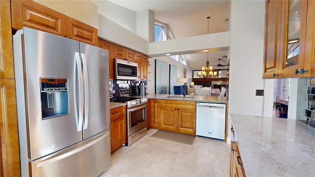 kitchen with a sink, appliances with stainless steel finishes, brown cabinetry, glass insert cabinets, and a chandelier