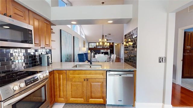 kitchen with a sink, tasteful backsplash, stainless steel appliances, a peninsula, and a chandelier